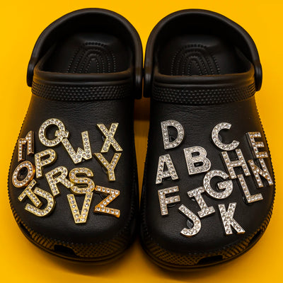 Black clogs with letter shoe charms on a yellow background
