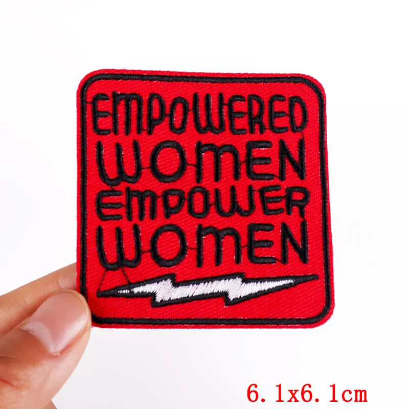 Red patch with 'EMPOWERED WOMEN EMPOWER WOMEN' text held by a hand on a white background