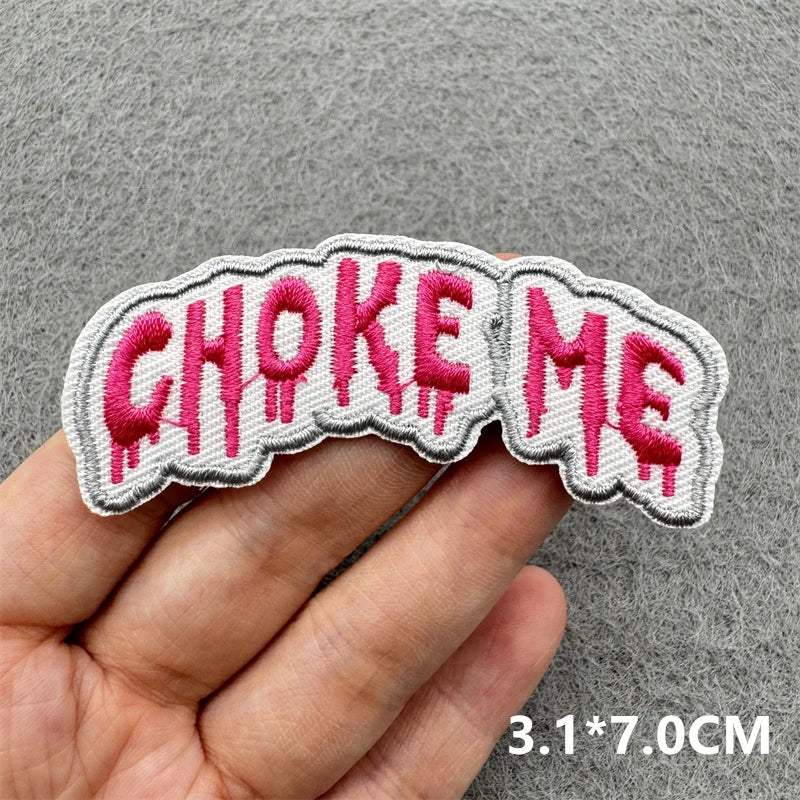 Embroidered patch with 'CHOKE ME' text held by a hand on a gray background