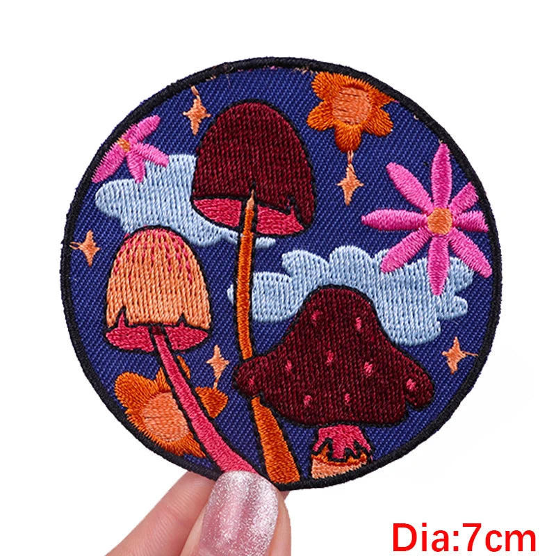 Circular embroidered patch with mushrooms and flowers held by a hand, labeled 'Diameter: 7cm'.
