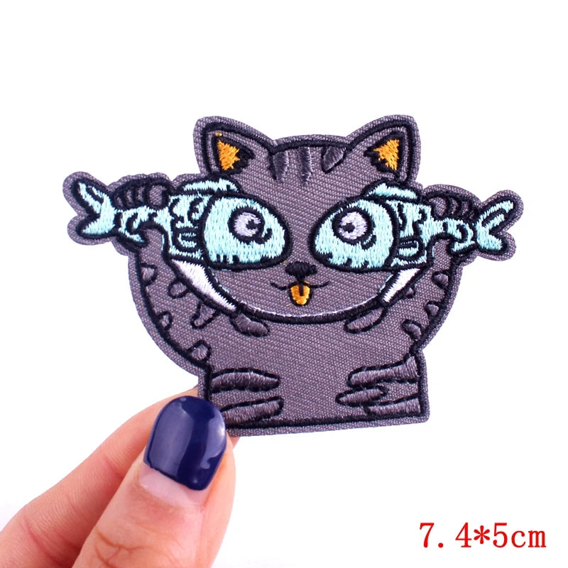 Embroidered patch of a cat with fish for eyes held by a hand on a white background