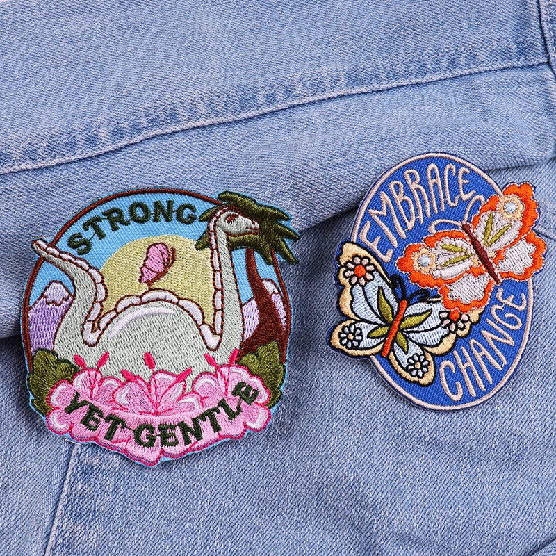 Two embroidered patches on a denim jacket, one with a dragon and the other with a butterfly and text.