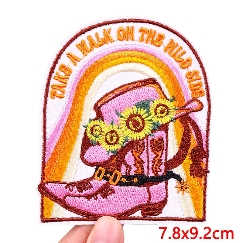 Embroidered patch with pink boot, rainbow, and text 'Take a walk on the wild side' held by a hand.