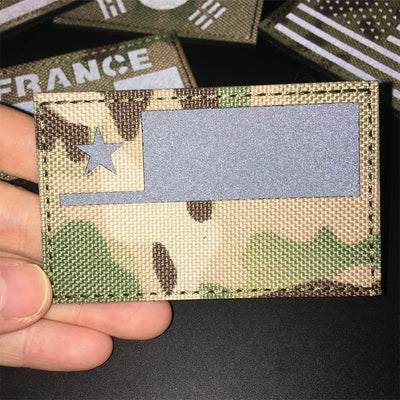 Camouflage patch with a flag held by a hand on a dark background