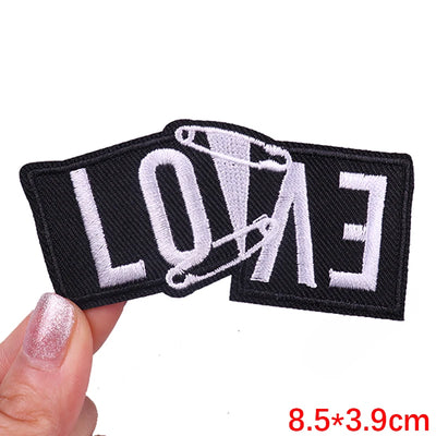Black patch with 'LOVE' and a safety pin held by a hand on a white background