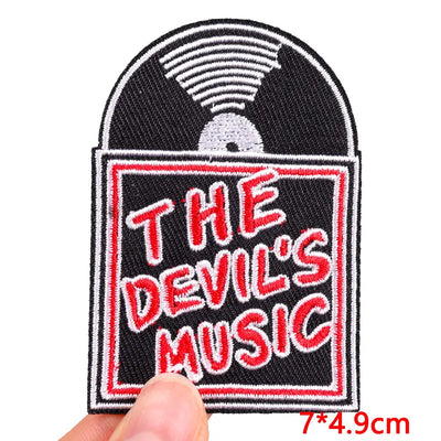 Patch with 'The Devil's Music' text held by a hand on a white background
