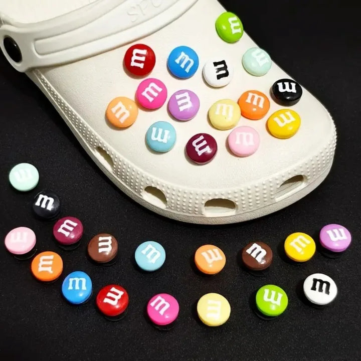 White clog shoe with colorful M&amp;M-themed buttons on a black background