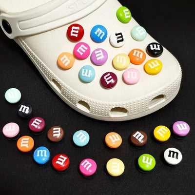 White clog shoe with colorful M&M-themed buttons on a black background
