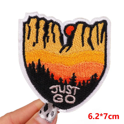 Embroidered patch with sunset design and 'JUST GO' text held by a hand, with size label '6.2*7cm'.