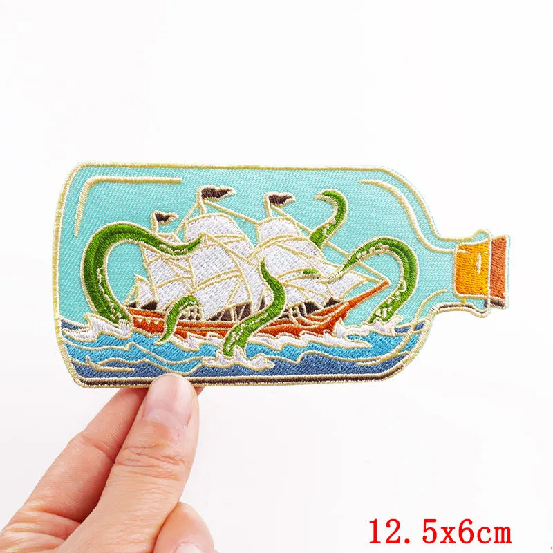 Embroidered patch of a ship in a bottle held by a hand on a white background