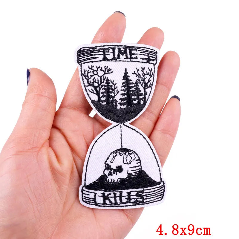 Hourglass patch with nature and skull design held in a hand, on a white background