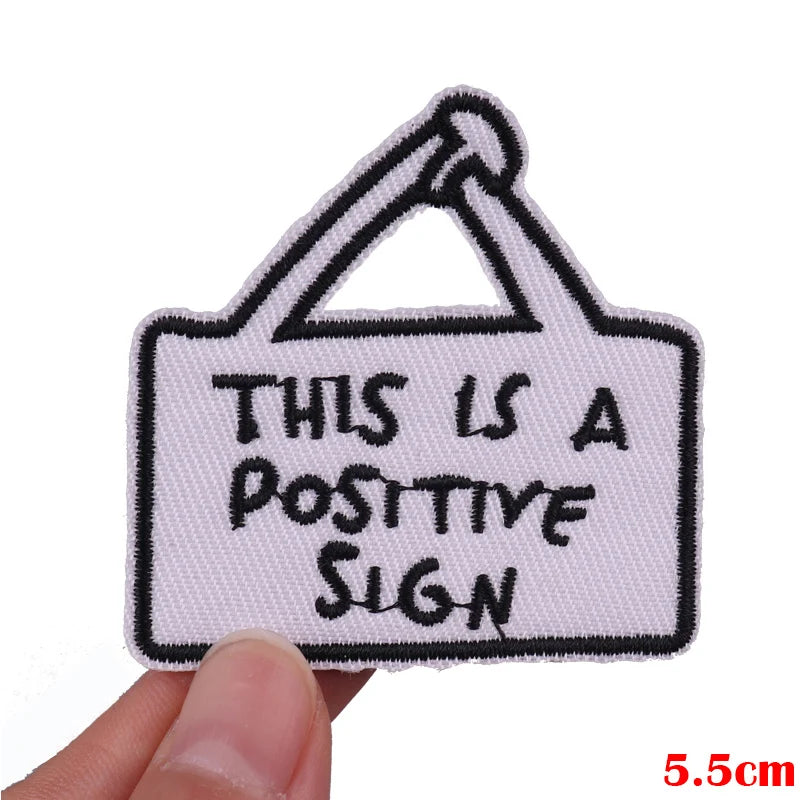 Embroidered patch with 'This is a positive sign' text held by a hand on a white background.