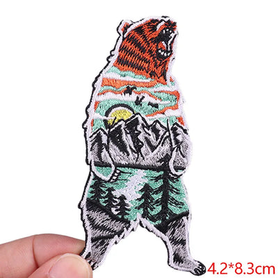 Embroidered patch of a bear with mountain design held by a hand on a white background