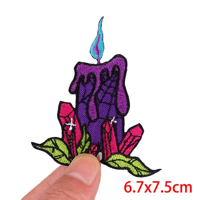 Colorful embroidered patch of a candle with hands holding it, held by a finger on a white background.