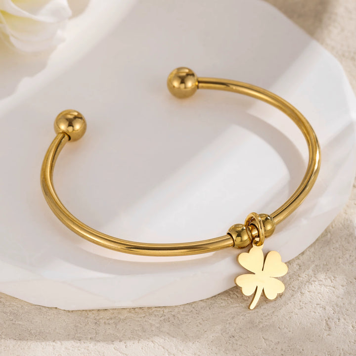Gold bracelet with a four-leaf clover charm on a white fabric background