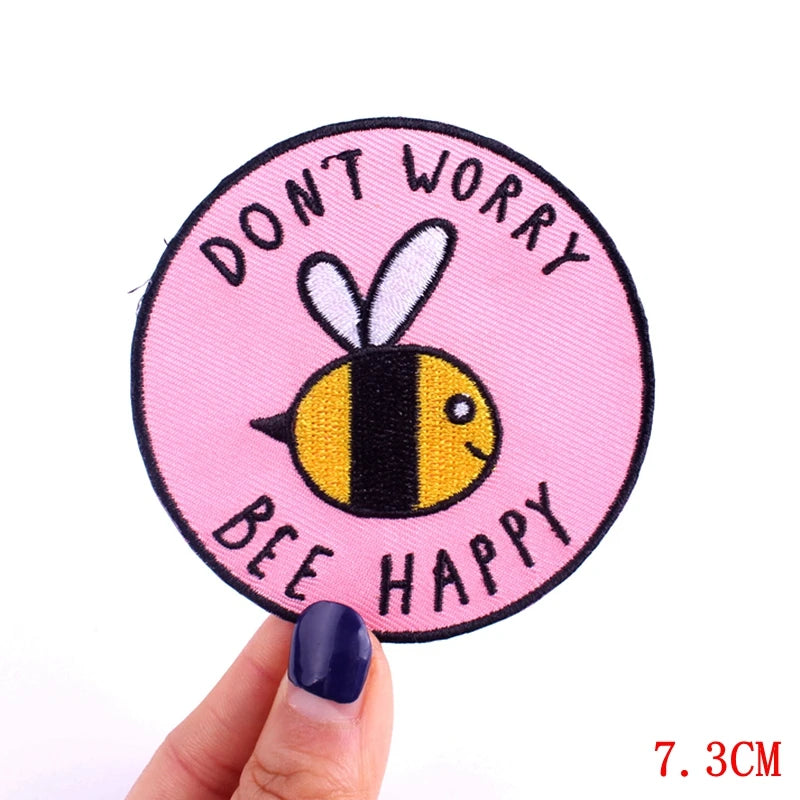 Circular patch with bee illustration and text 'Don't Worry, Bee Happy' held by a hand.