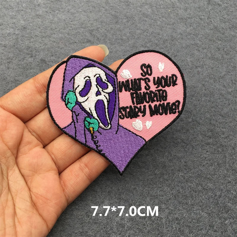 Heart-shaped patch with a ghost face design and text held by a hand on a gray background