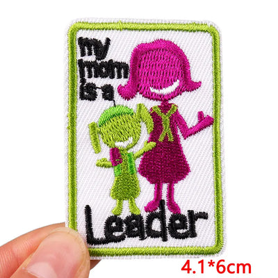 Embroidered patch with cartoon characters and text 'my mom is a Leader' held by a hand.