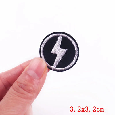 Black and white lightning bolt patch held between fingers with size label '3.2x3.2cm' on a white background