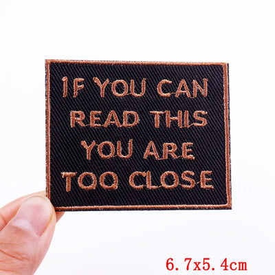 Text patch with 'IF YOU CAN READ THIS YOU ARE TOO CLOSE' message held by a hand, with dimensions displayed.