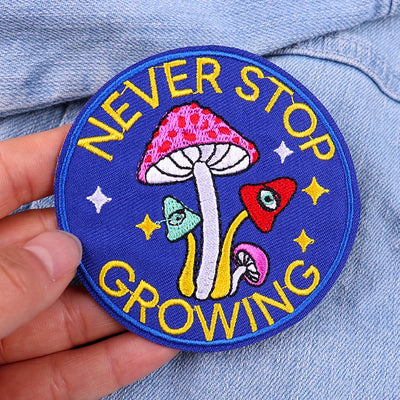 Patch with mushrooms and 'Never Stop Growing' text held over a denim background