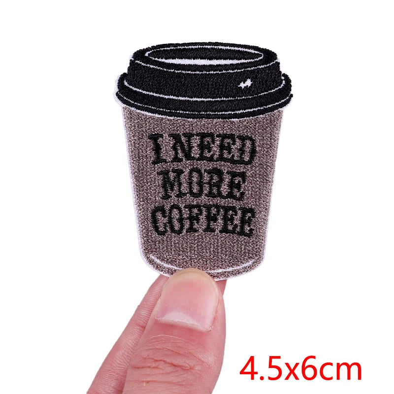 Coffee cup sleeve with 'I Need More Coffee' text held by a finger, on a white background.