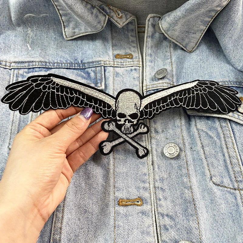 Hand holding a skull and crossbones patch with wings against a denim jacket.