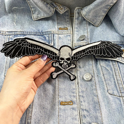Hand holding a skull and crossbones patch with wings against a denim jacket.
