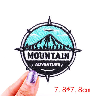 Mountain adventure patch held by a hand with purple nail polish on a white background
