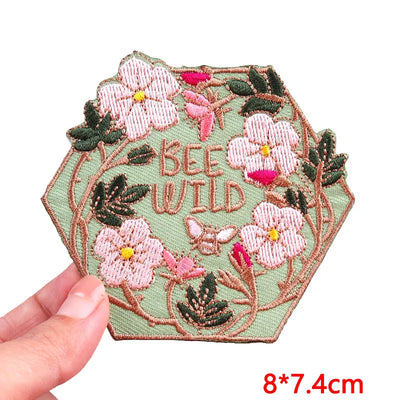Embroidered patch with flowers and 'BEE WILD' text held by a hand on a white background.