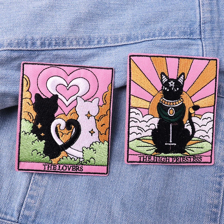Two embroidered patches of cats in tarot card style on a denim background