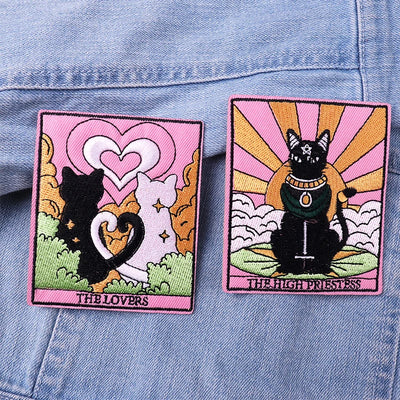 Two embroidered patches of cats in tarot card style on a denim background