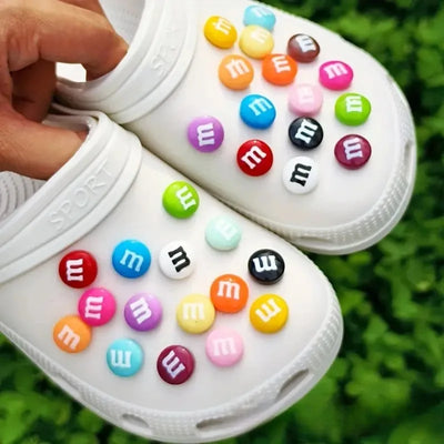 White clogs with colorful M&M-themed buttons on a grass background