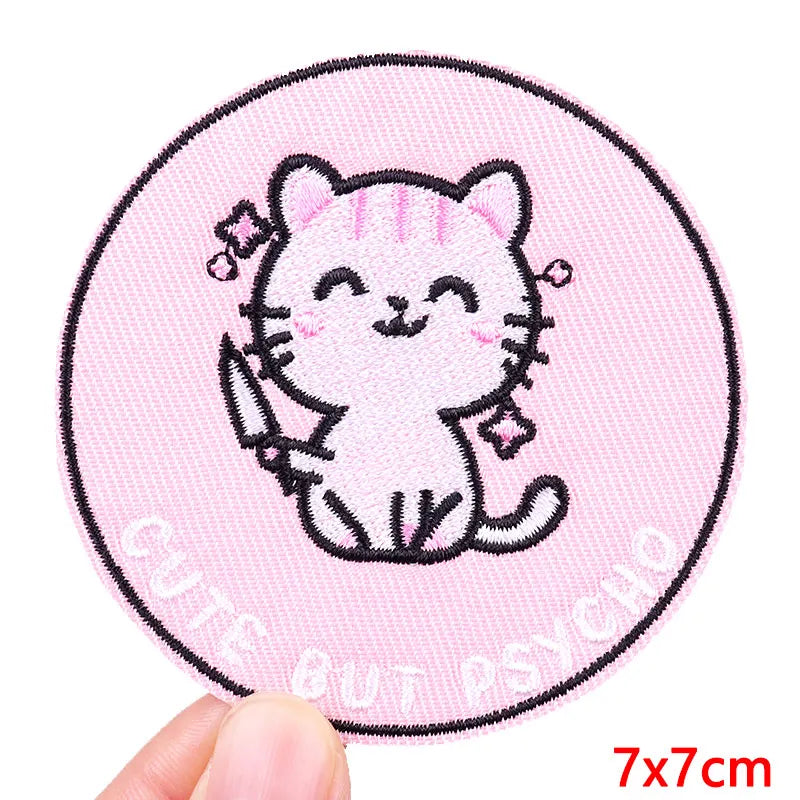 Circular patch with a cartoon cat design on a pink background, held by a hand.