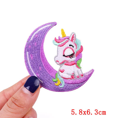 Embroidered patch of a unicorn on a purple crescent moon held by a hand.