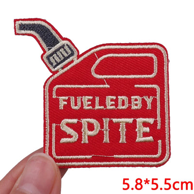 Embroidered patch with 'Fueled by Spite' text on a red background, held by a hand.