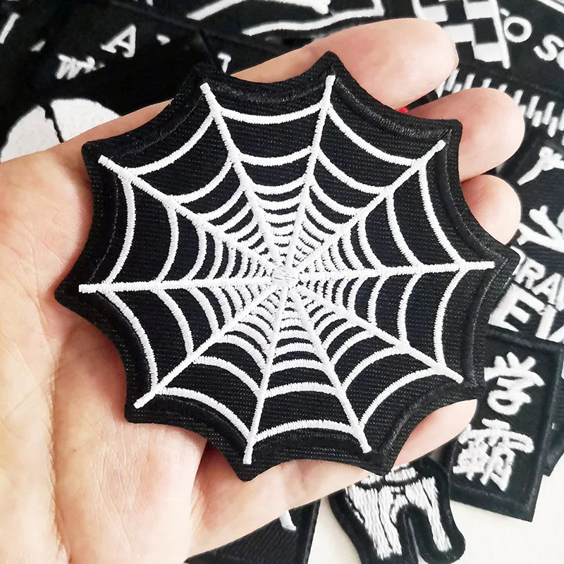 Black spider web patch held in a hand with other patches in the background