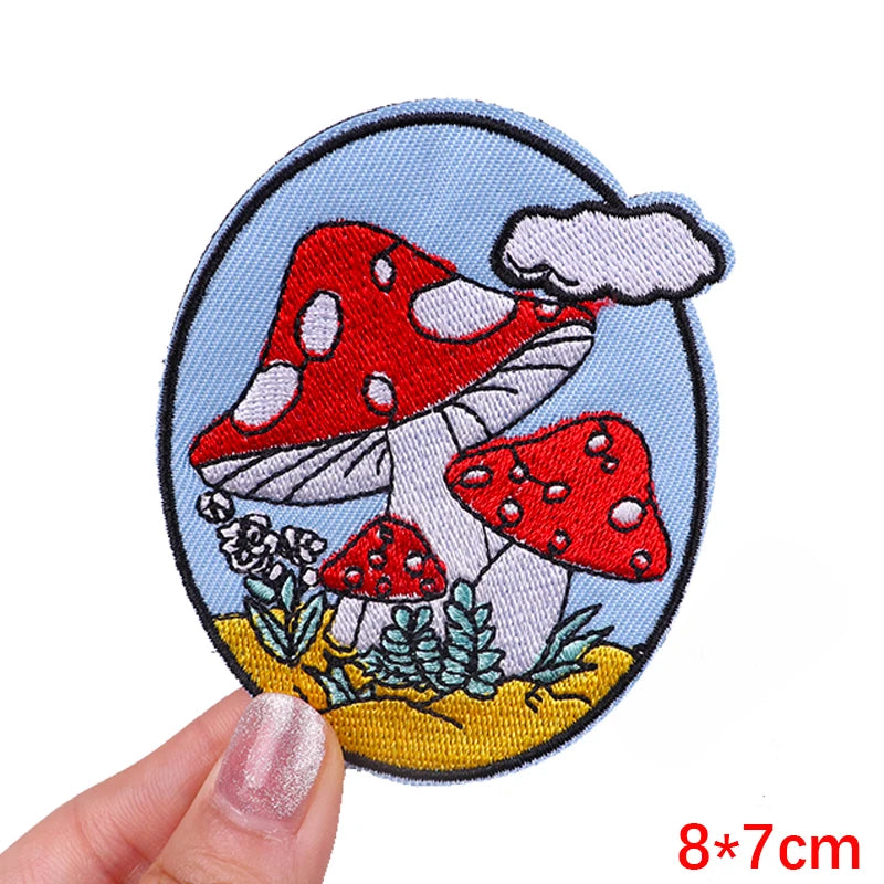 Embroidered patch with red mushrooms held by a hand on a white background