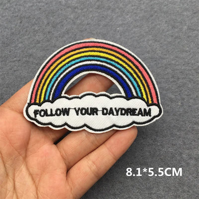 Patch with rainbow and 'Follow Your Daydream' text held in a hand on a gray background