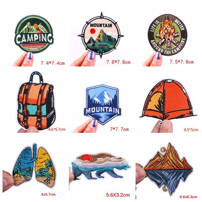 Collection of camping-themed patches with measurements held by fingers on a white background.