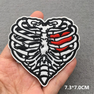 Heart-shaped patch with skeleton design held by a hand on a gray background