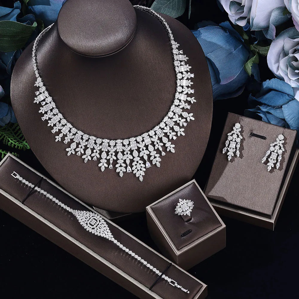 Jewelry set including necklace, earrings, ring and bracelet on a dark surface with flowers in the background.