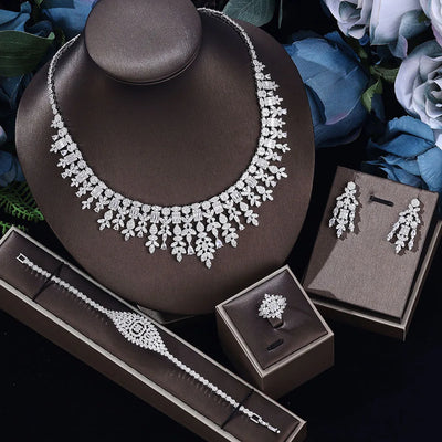 Jewelry set including necklace, earrings, ring and bracelet on a dark surface with flowers in the background.
