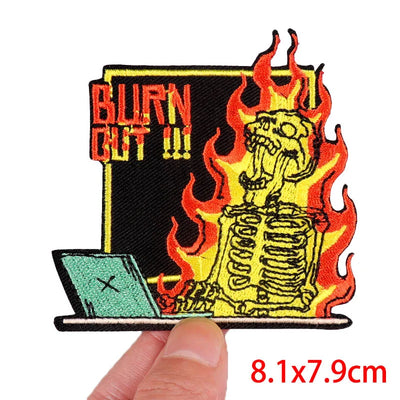 Embroidered patch with skeleton, flames, and 'Burn Out' text held by a hand.