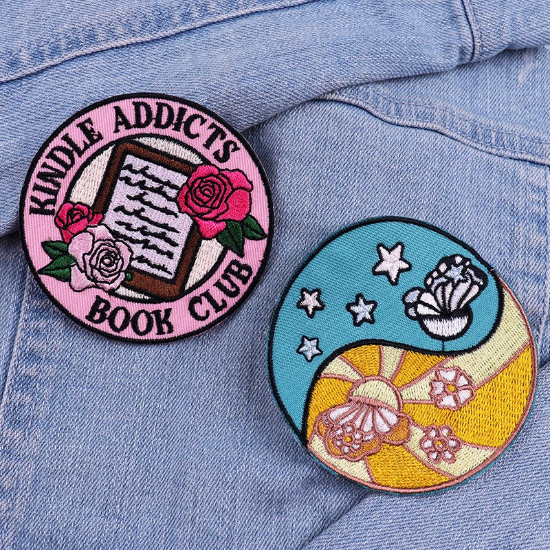 Two embroidered patches on a denim jacket, one labeled 'Kindle Addicts Book Club' with roses and an open book, the other with a butterfly and stars design.