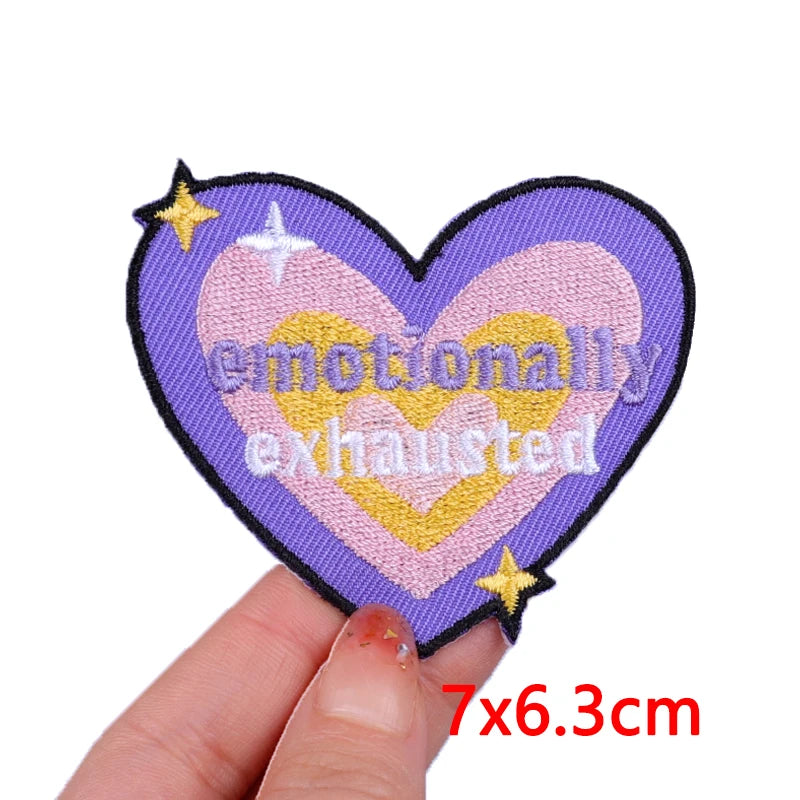 Heart-shaped patch with 'emotionally exhausted' text held by a hand on a white background