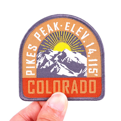 Patch with Pikes Peak and Colorado text held by a hand on a white background