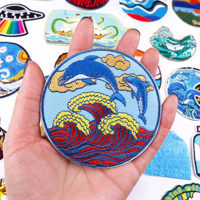 Hand holding a patch with dolphins and waves against a background of various other patches.