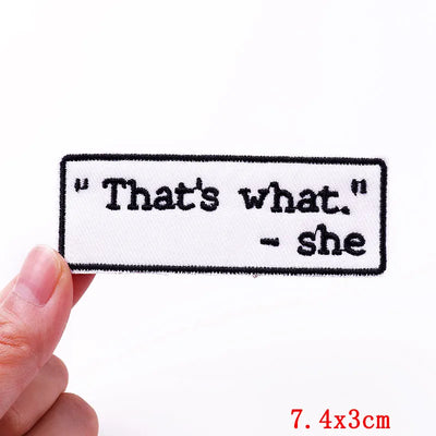 Embroidered patch with text 'That's what. she' held by a hand on a white background