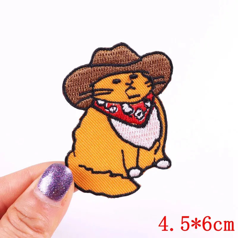 Embroidered patch of a cartoon cat in a cowboy hat held by a hand with purple nail polish.